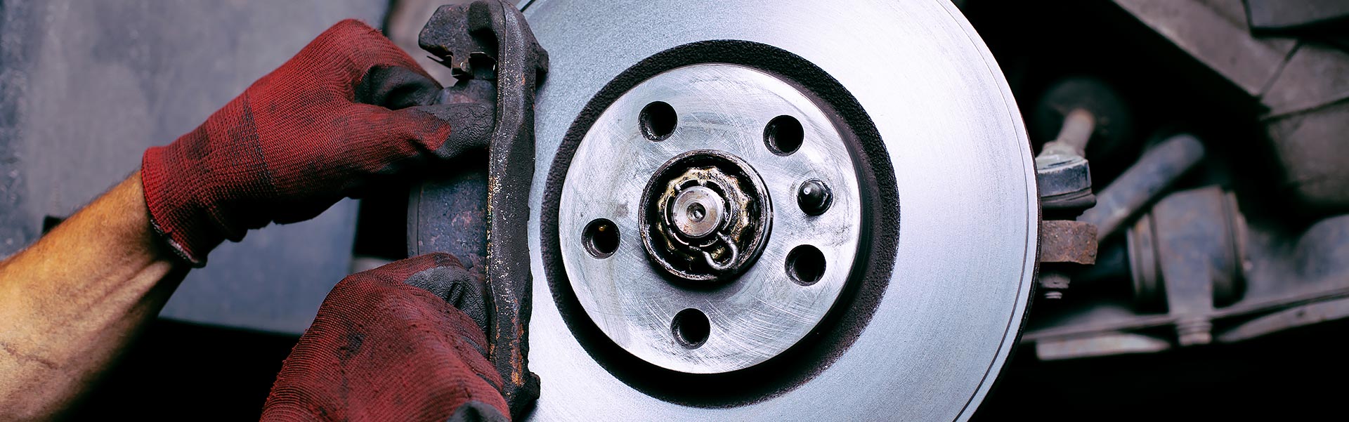 mechanic in red gloves installing a brake pad onto a shiny car disc brake rotor